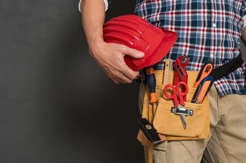 Plastering Subcontractor construction worker with tool belt and red helmet