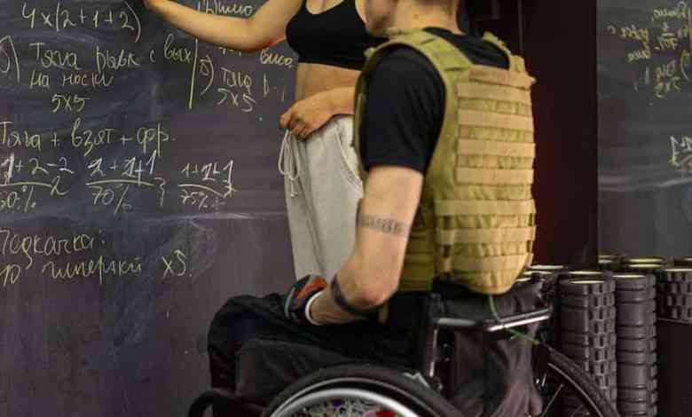 a man sitting on a wheelchair while listening to the woman writing on the board