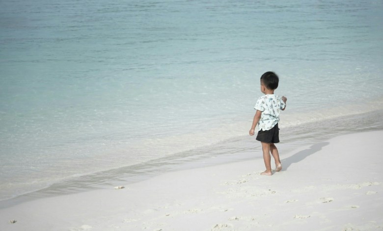 a young boy standing on top of a sandy beach