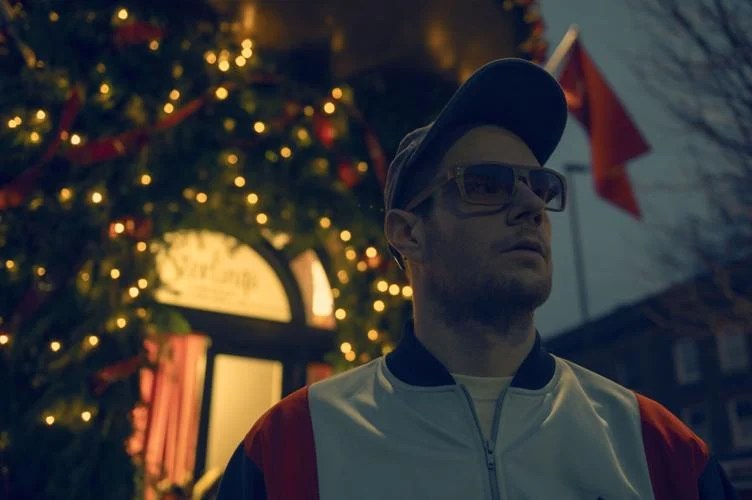 A close-up cinematic shot of a character from Jingle Bell Heist standing in front of blurred Christmas lights and decorations.