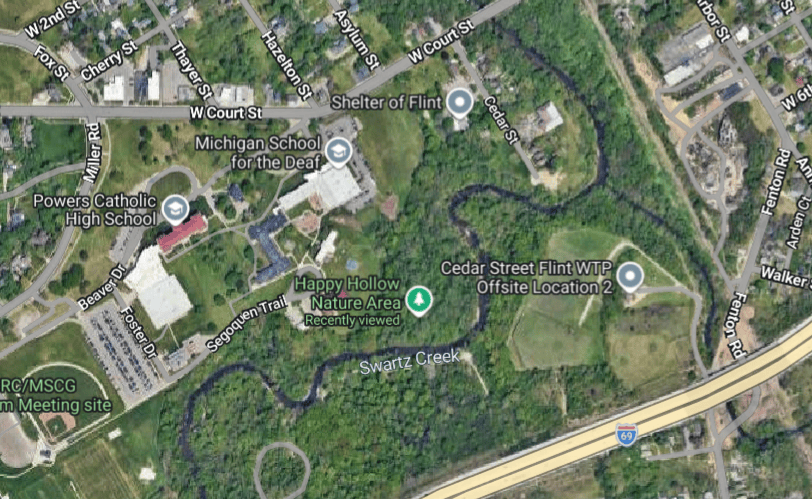 Aerial view of a neighborhood featuring several landmarks including Powers Catholic High School, Michigan School for the Deaf, and the Shelter of Flint, alongside Swartz Creek and nearby nature areas.