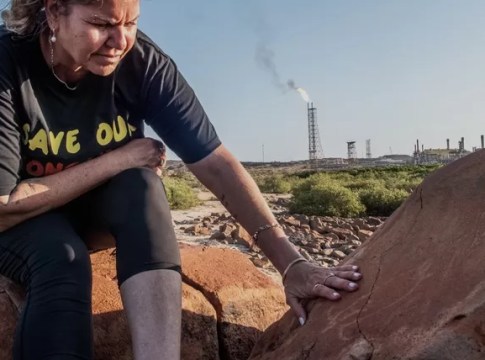 Raelene Cooper and an ancient Turtle Petroglyph with a flaring gas facility behind them