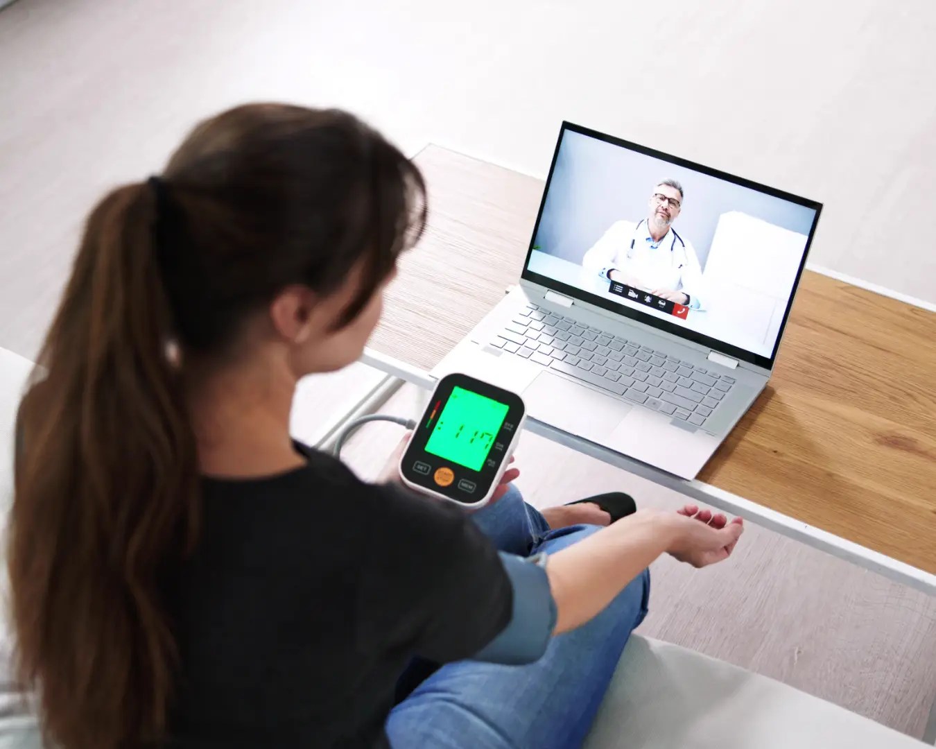 Young female patient testing blood pressure over a zoom call with doctor.