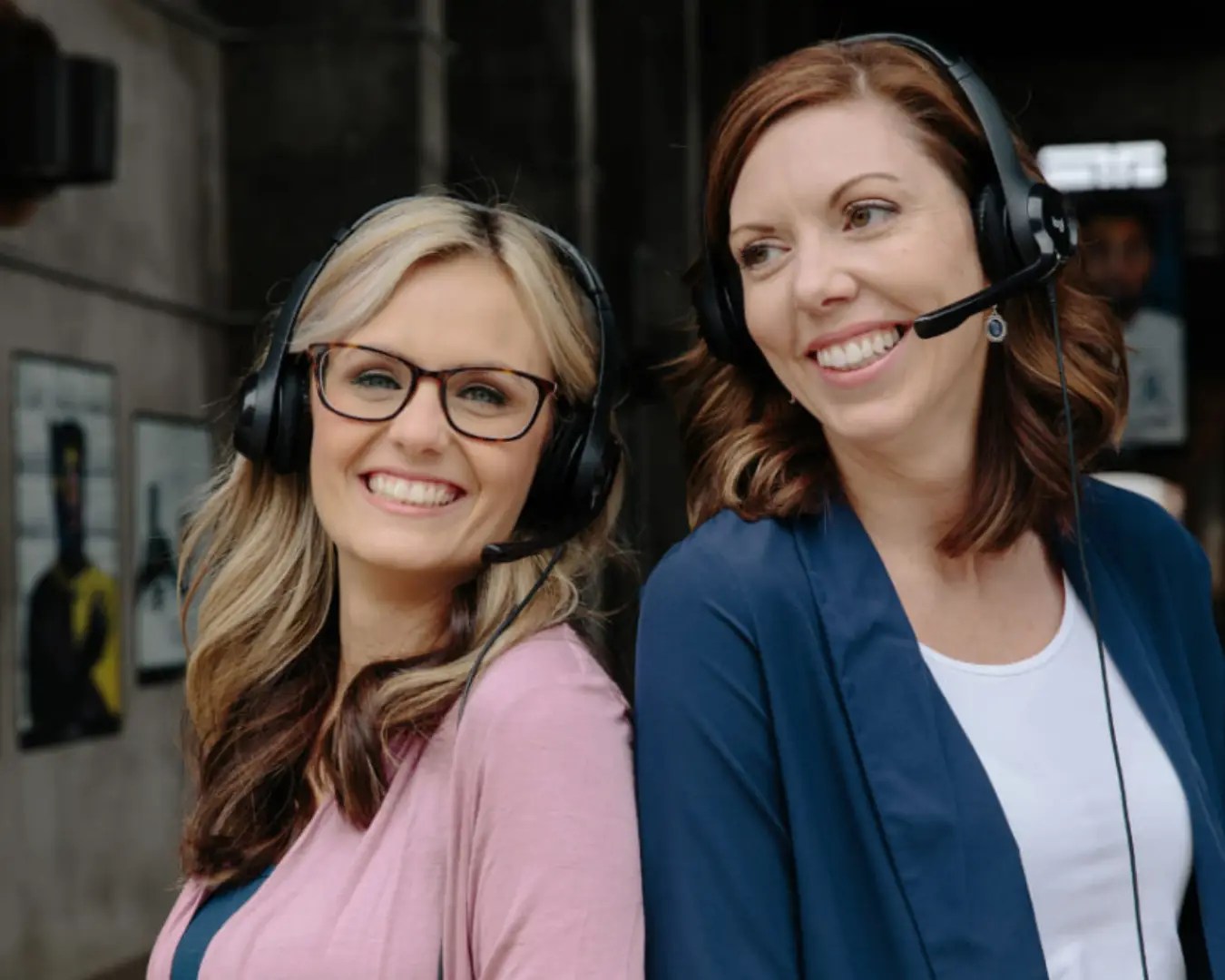 Co-founder, Cayce Branyon and Emily Smith, back to back, outside, wearing phone headsets, smiling on a sunny day.