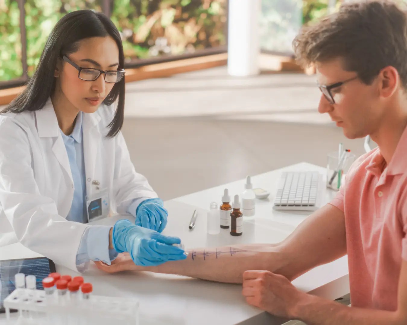 Young female allergist performing allergy test on young man holding his arm out.