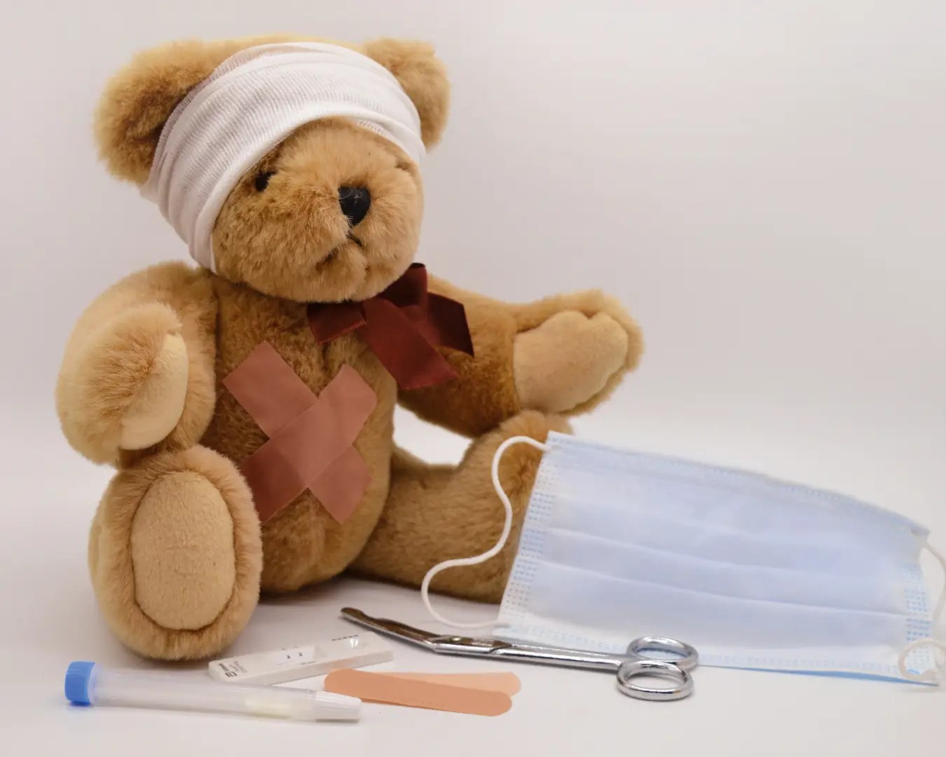 Teddy bear with bandage on head, sitting on table next to medical equipment and mask.
