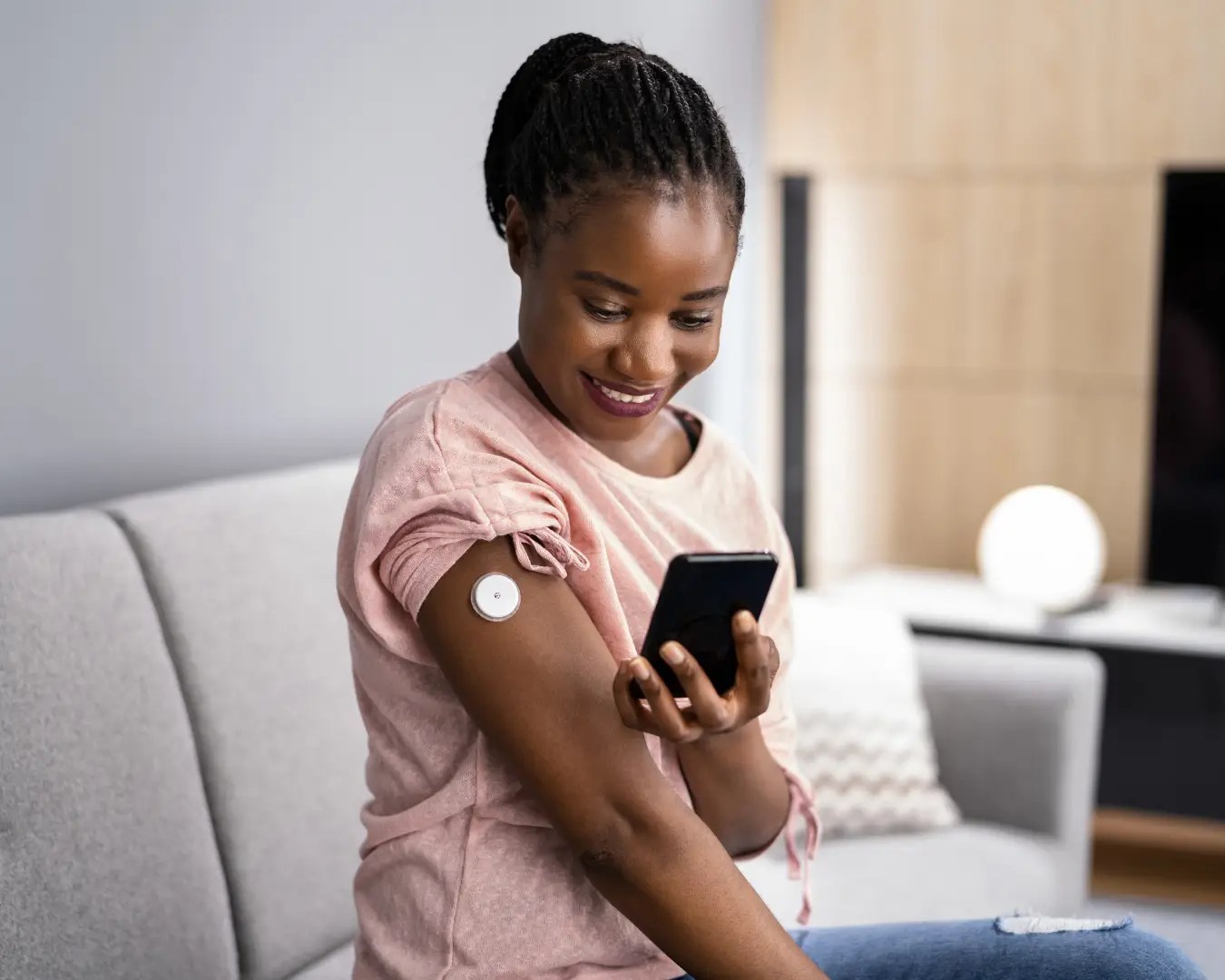 Young Black adult female sitting at home on her couch with RPM device on arm, smiling at home.