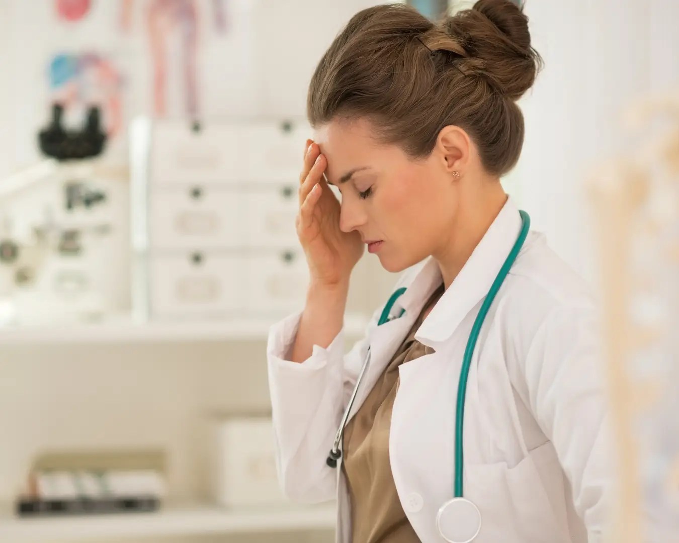 Female doctor in office, with hand on forward, looking burned out.