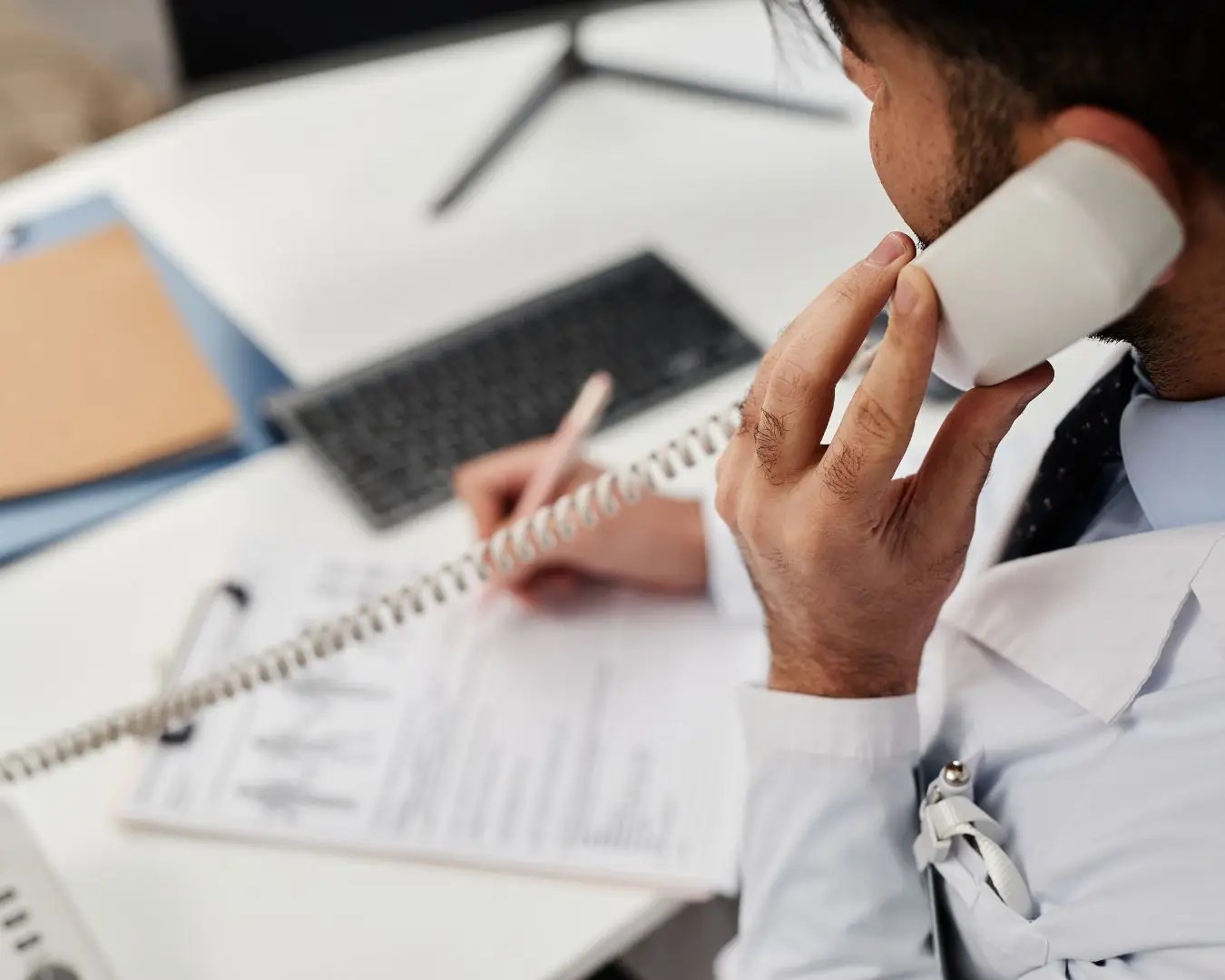 Close up shot from behind of doctor on phone, writing down on documents.
