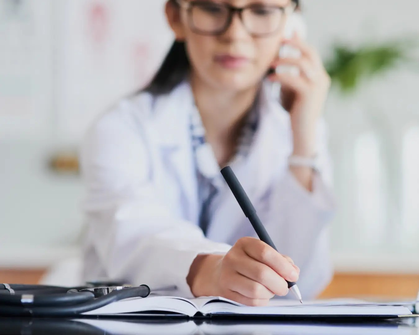 Female doctor on phone writing down on notepad in medical office.