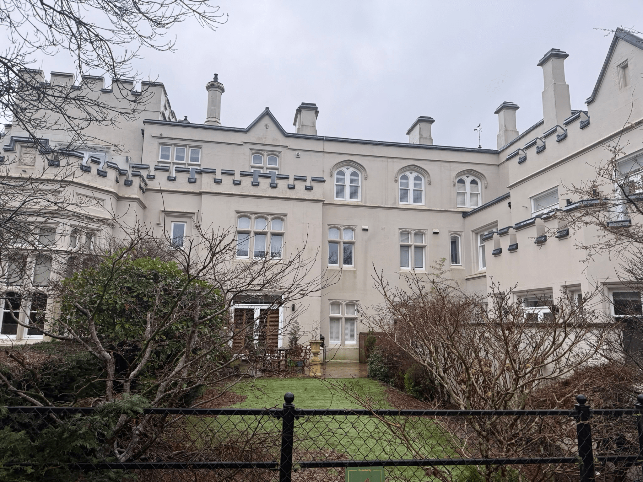 Rear elevation of a historic cream-coloured residential building with Gothic-style windows, landscaped garden and courtyard.