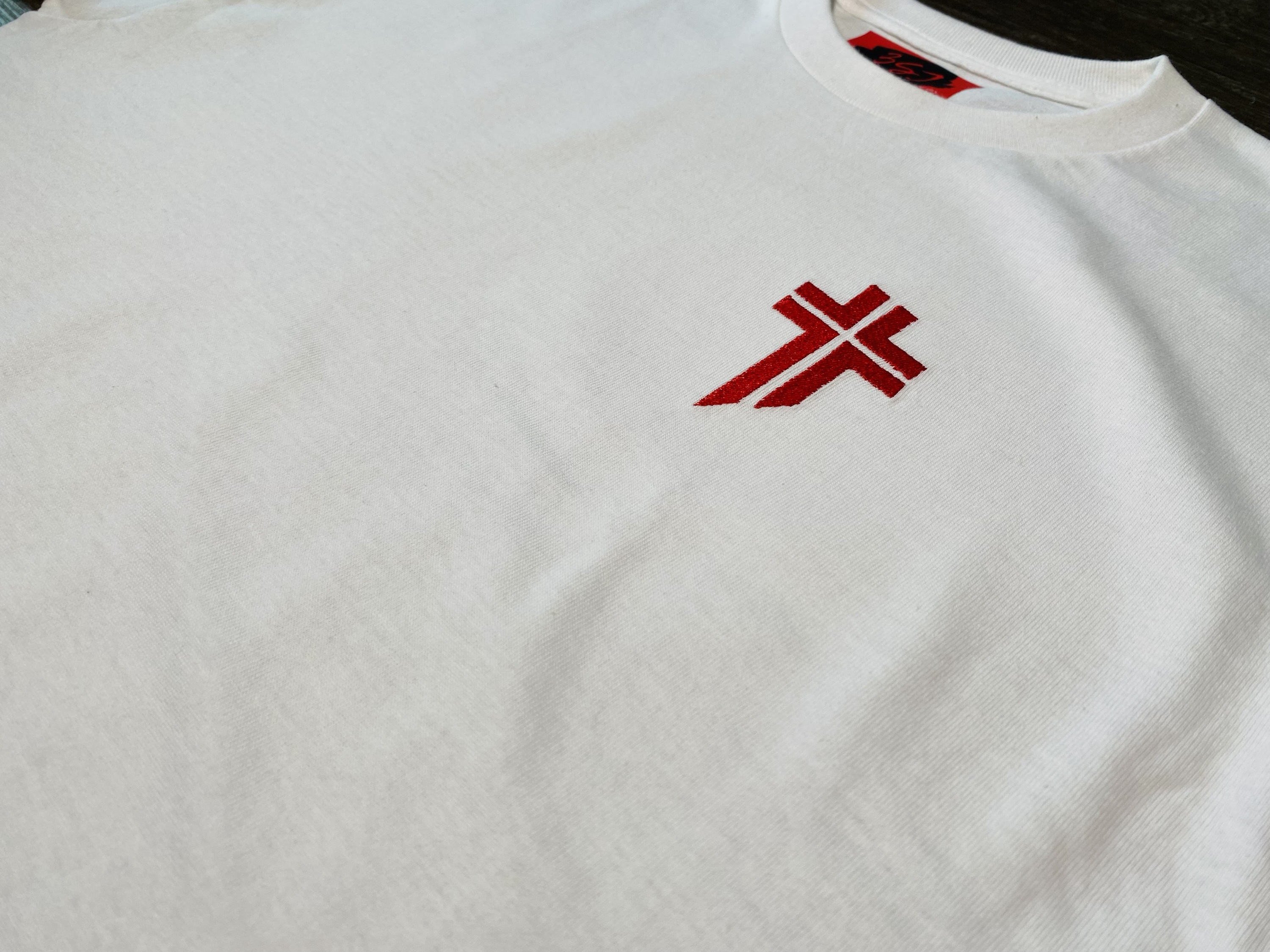 Close-up of a white T-shirt with a red Lebanese Forces Cross embroidered on the left chest.