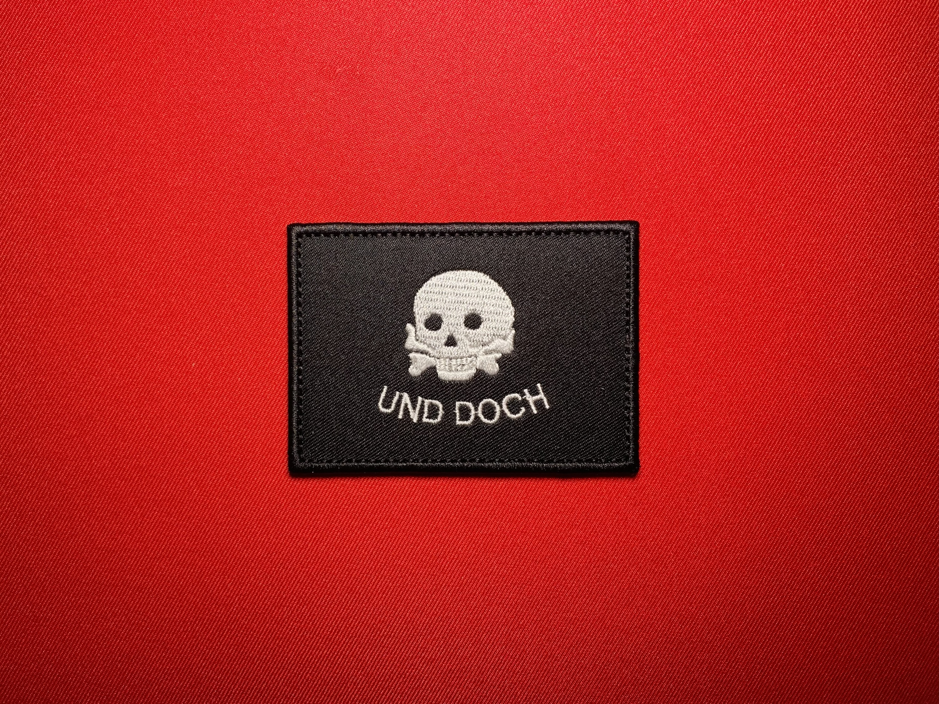 Black and white German Freikorps Iron Division “UND DOCH” embroidered patch featuring a Totenkopf-style skull and crossbones, historical 1919 Baltic campaign military reproduction insignia.