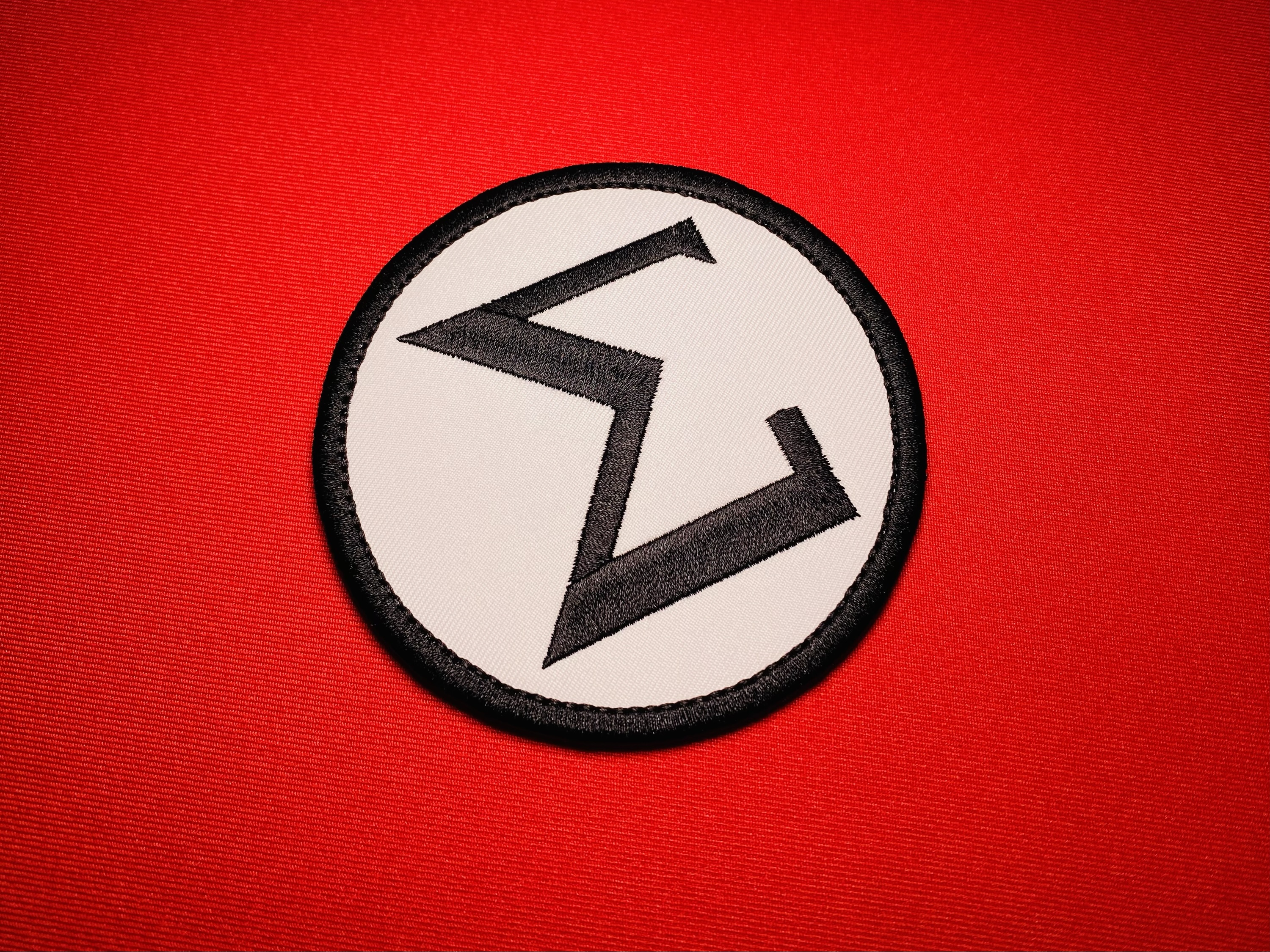 Close-up of a 4-inch Ação Integralista Brasileira (Brazilian Integralist Action) Sigma sleeve insignia with a black embroidered symbol on a white circular field and black border.