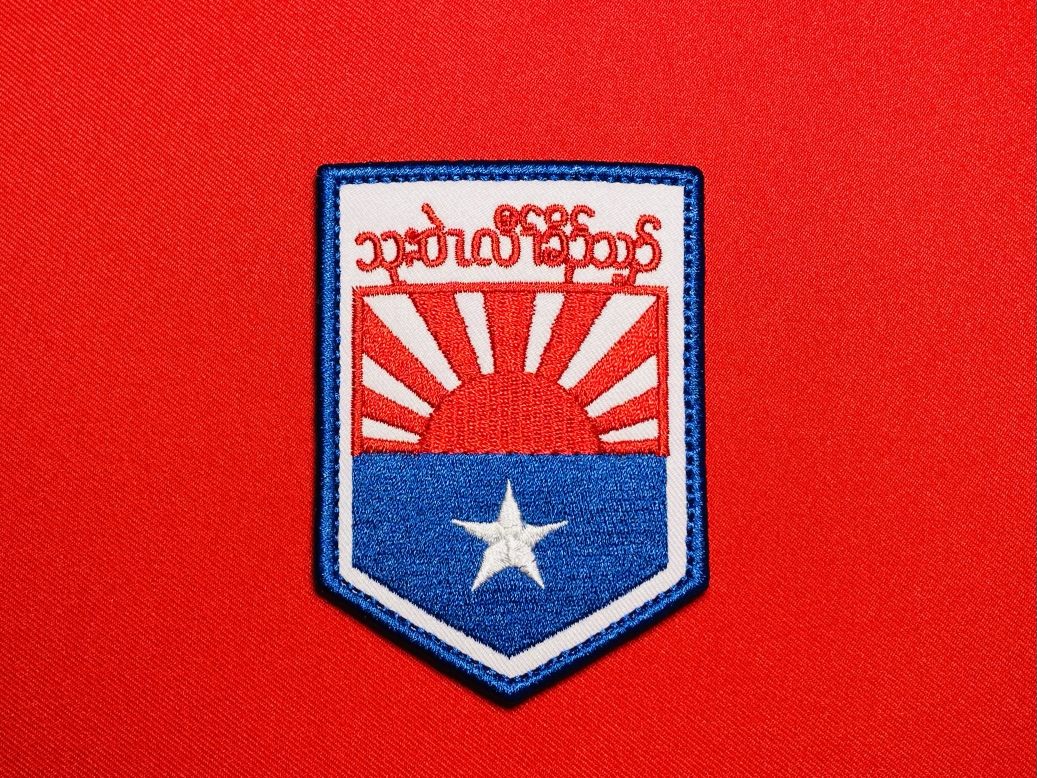 Front view of a reproduction KNLA Karen National Liberation Army Military Headquarters patch with S’gaw Karen lettering, red-and-white rising sun design, blue lower field, and white star.