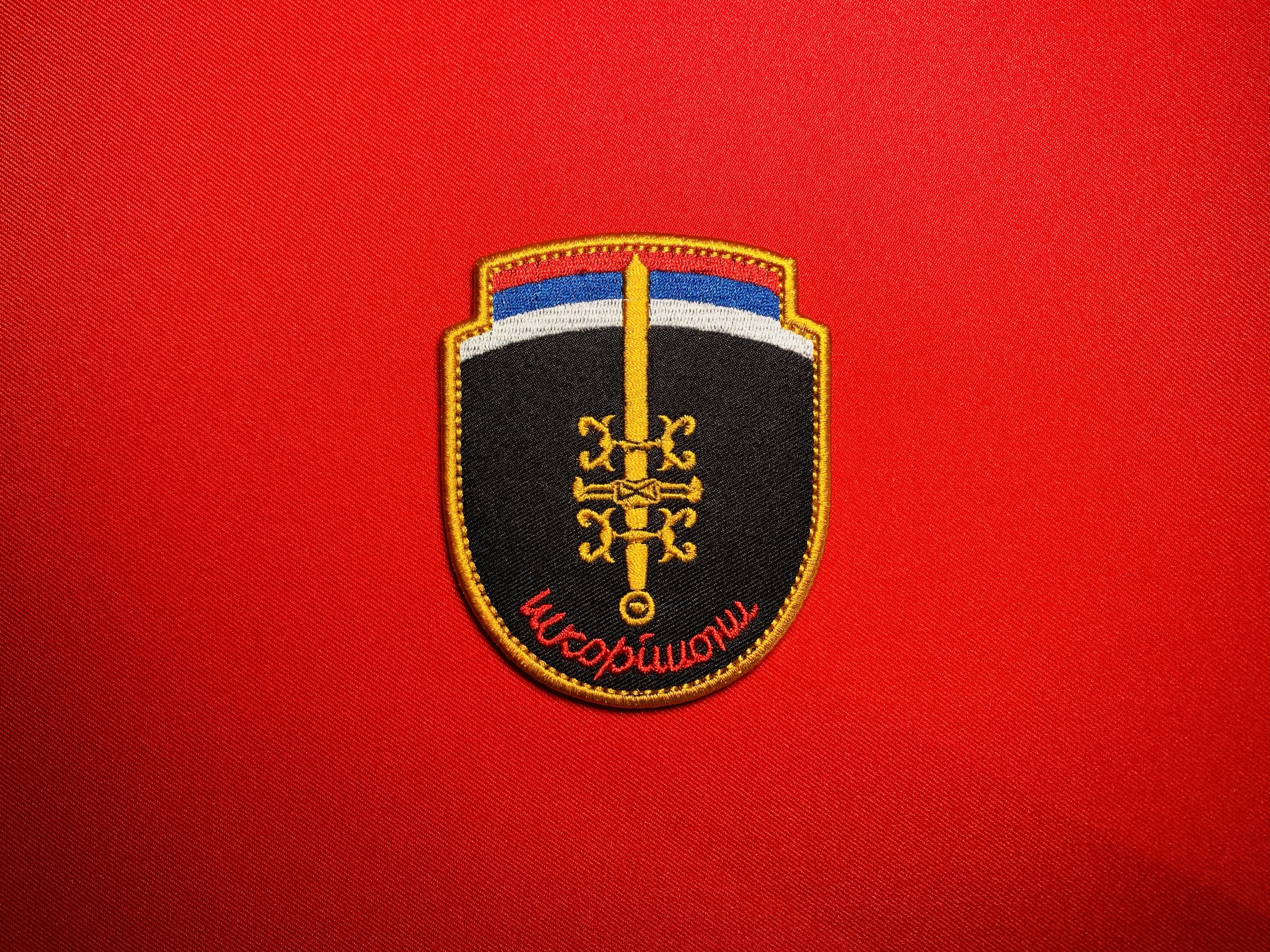 Front view of Serbian Škorpioni Scorpions sword insignia patch with Serbian flag colors, gold sword, ocila firesteels, and red Cyrillic lettering.