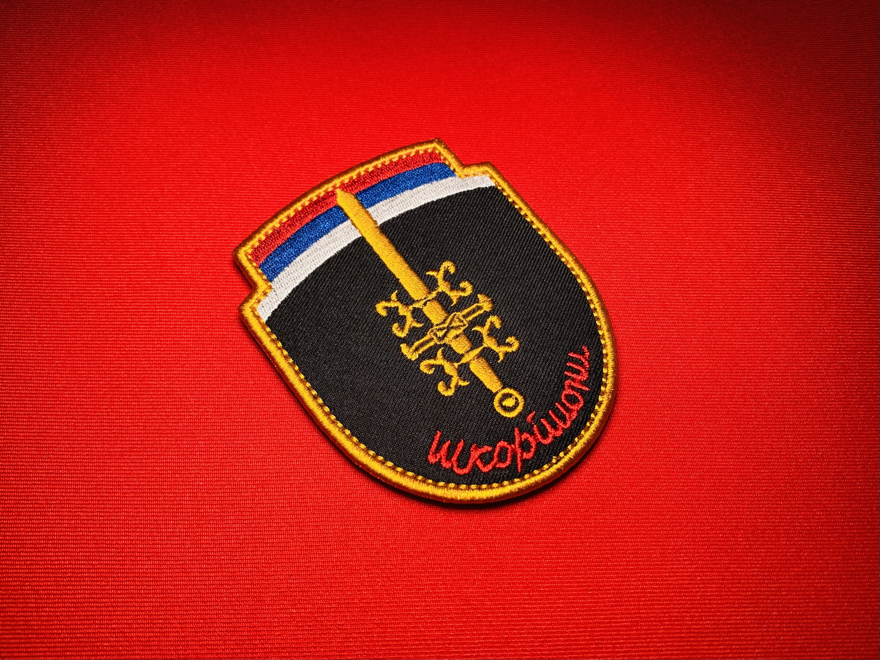 Serbian Škorpioni Scorpions sword patch with Serbian tricolor, gold sword, firesteels, and Cyrillic unit name on black shield.