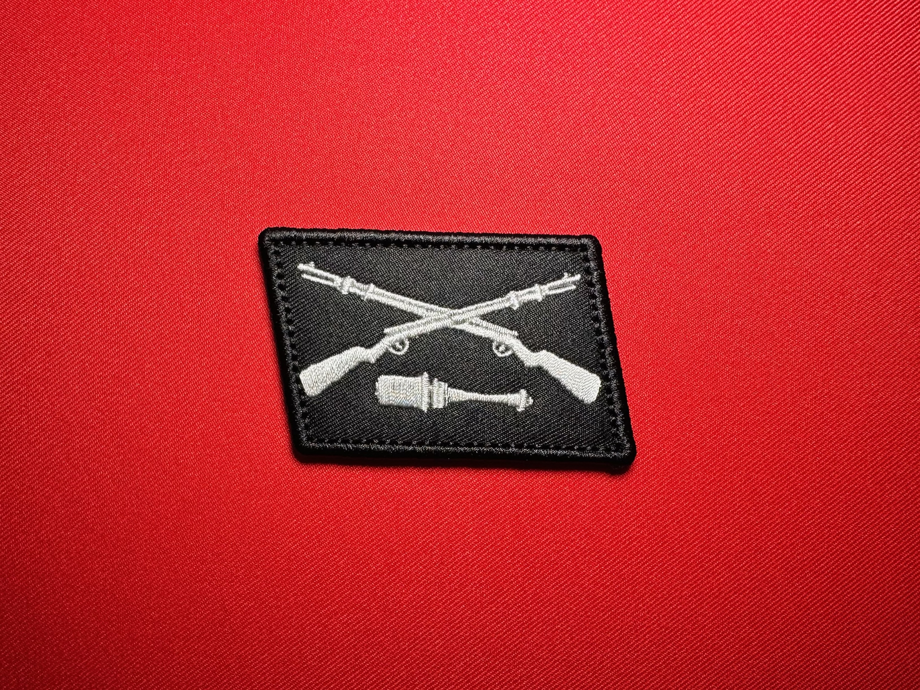 Black reproduction Dirlewanger collar tab featuring light gray crossed rifles above a horizontal stick grenade.
