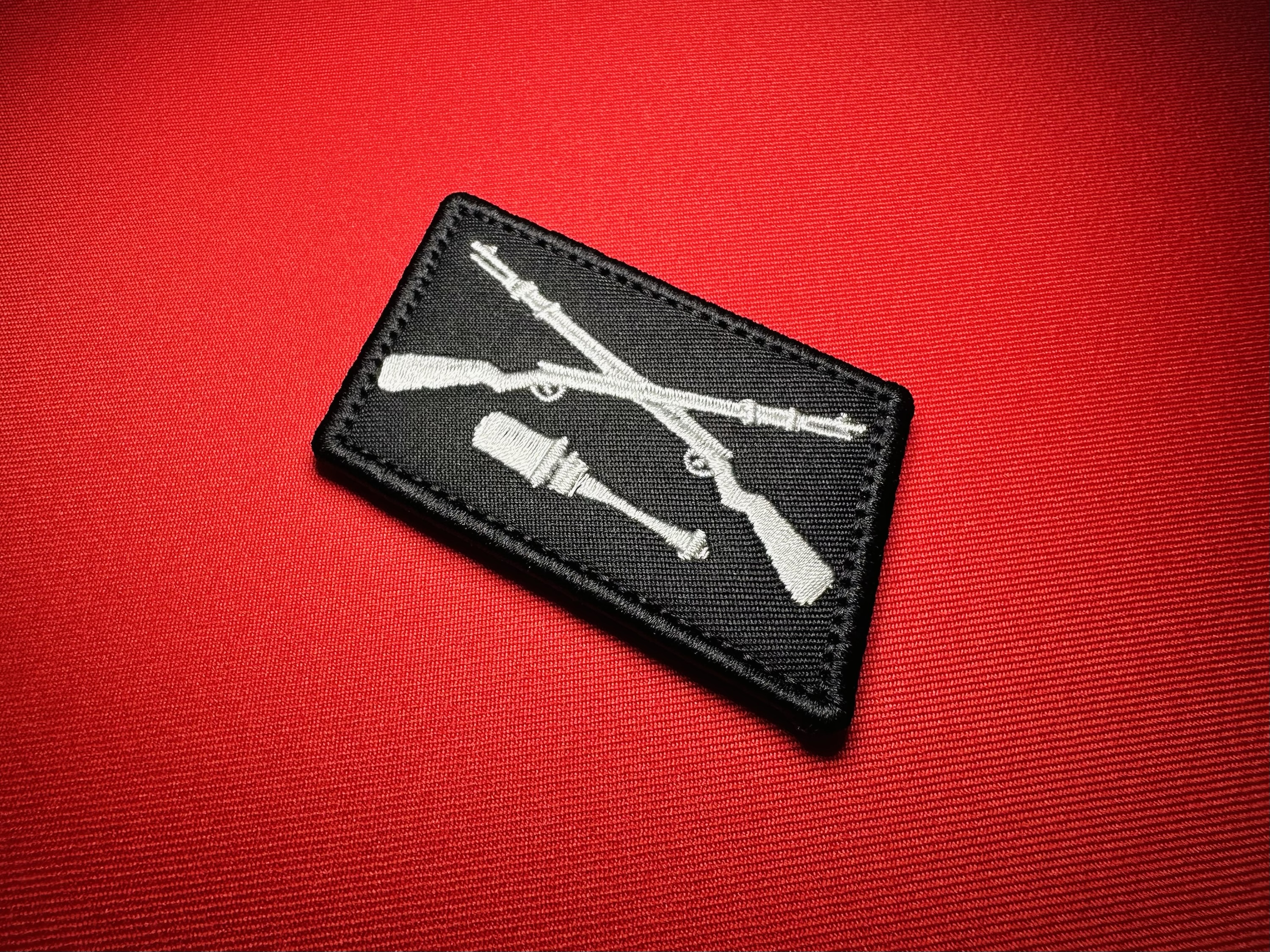 Black reproduction Dirlewanger collar tab featuring crossed rifles above a horizontal stick grenade.