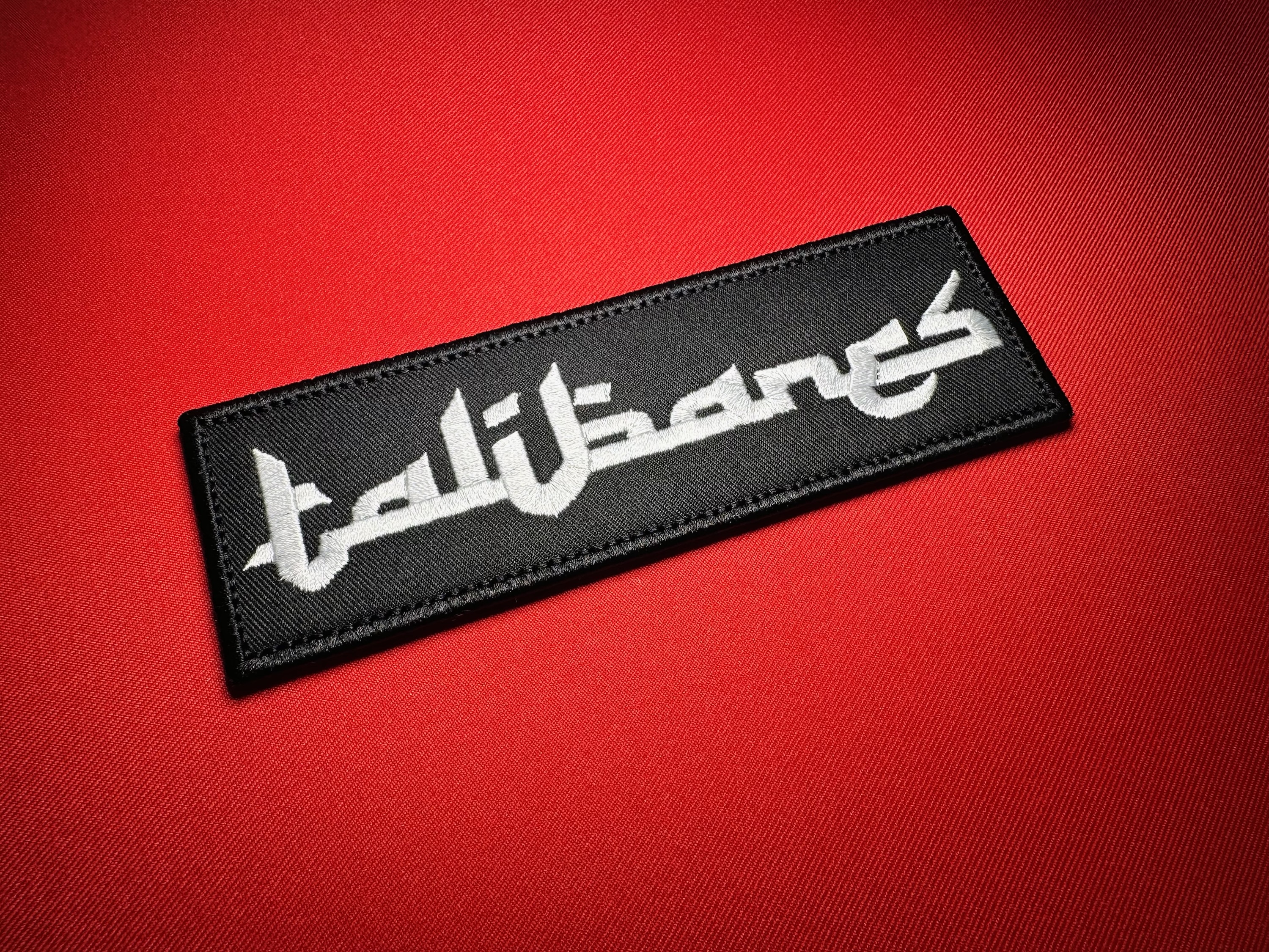 Los Talibanes replica embroidered chest patch, attributed to La Línea/Nuevo Cártel de Juárez (NCDJ), with white Arabic-inspired lettering on black fabric, shown at an angle.