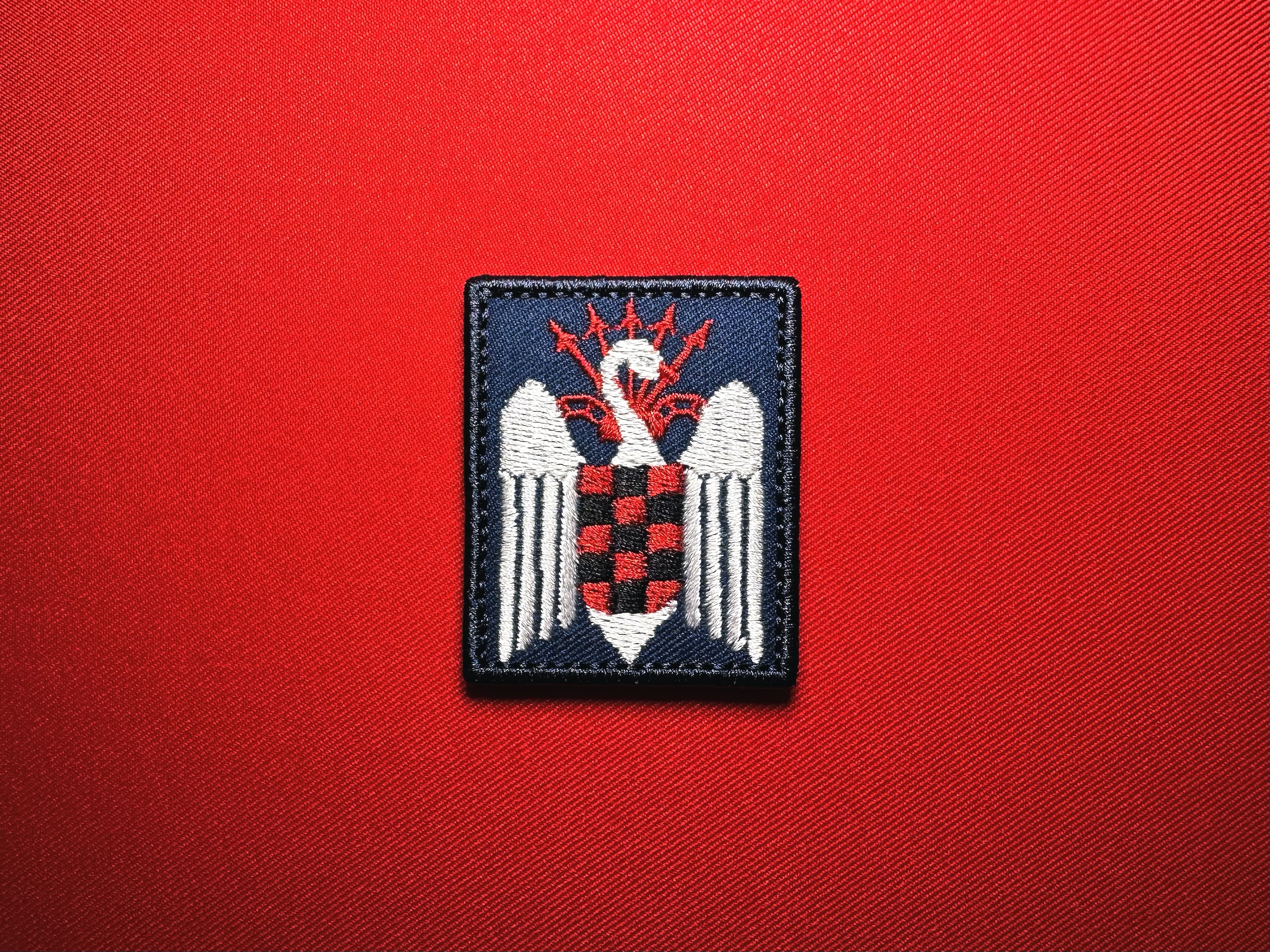 Reproduction Spanish Falanges Juveniles de Franco embroidered patch featuring a white swan, red-and-black checkered shield, and red yoke and arrows on dark blue fabric.