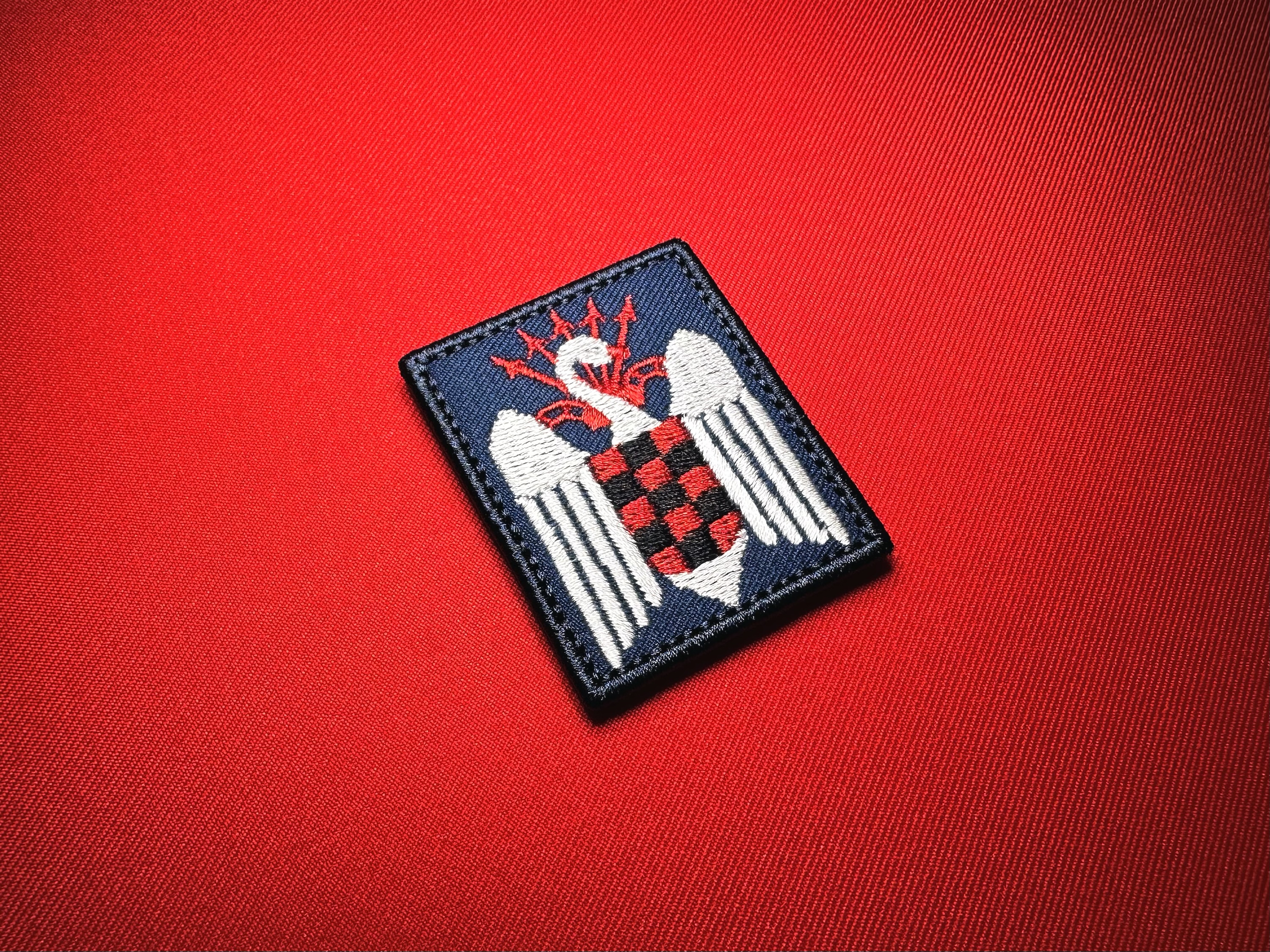 Reproduction Spanish Falanges Juveniles de Franco embroidered patch featuring a white swan, red-and-black checkered shield, and red yoke and arrows on dark blue fabric.
