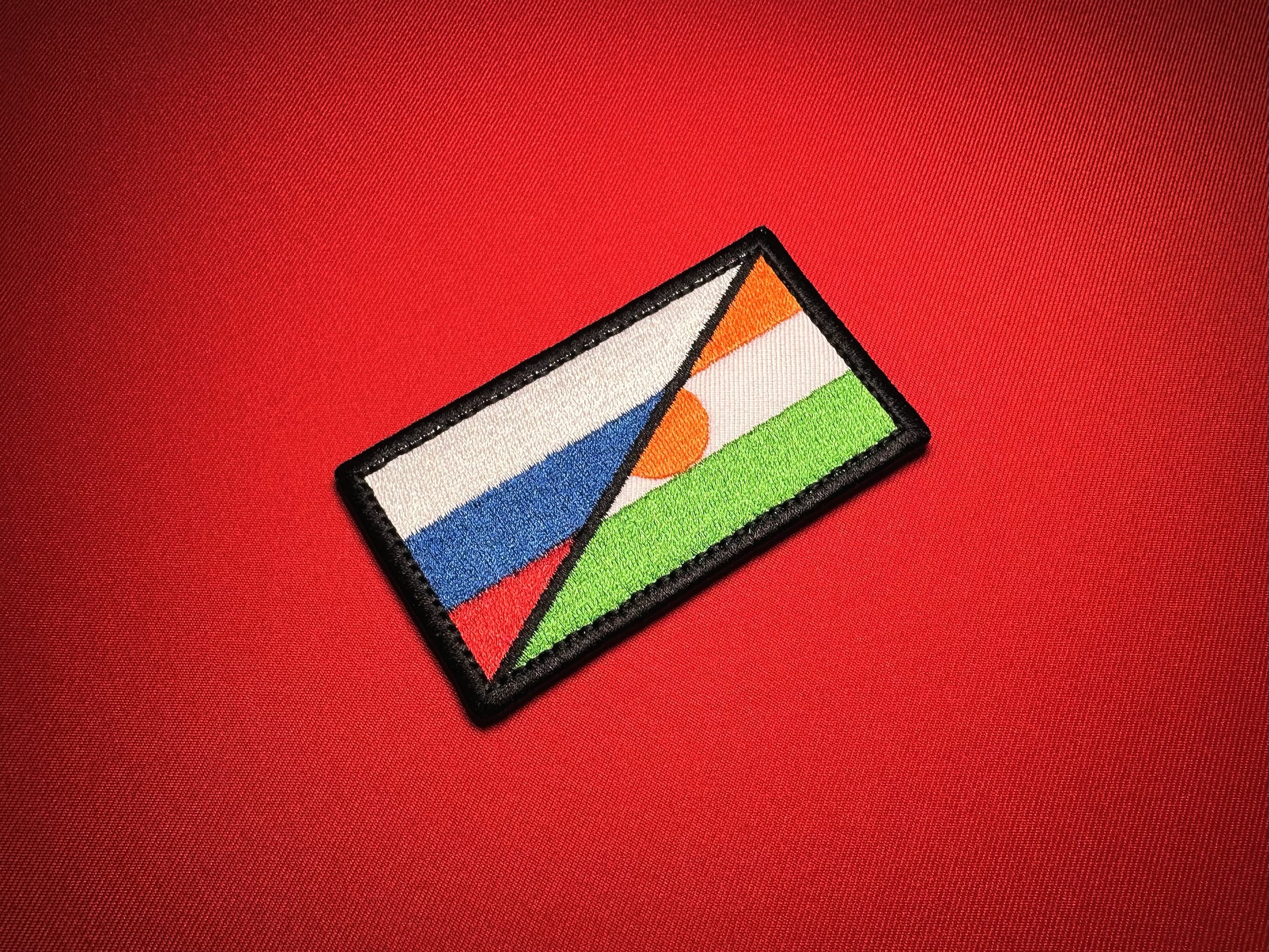 Angled view of a Russia–Niger cooperation flag replica patch with a black embroidered border on red fabric.