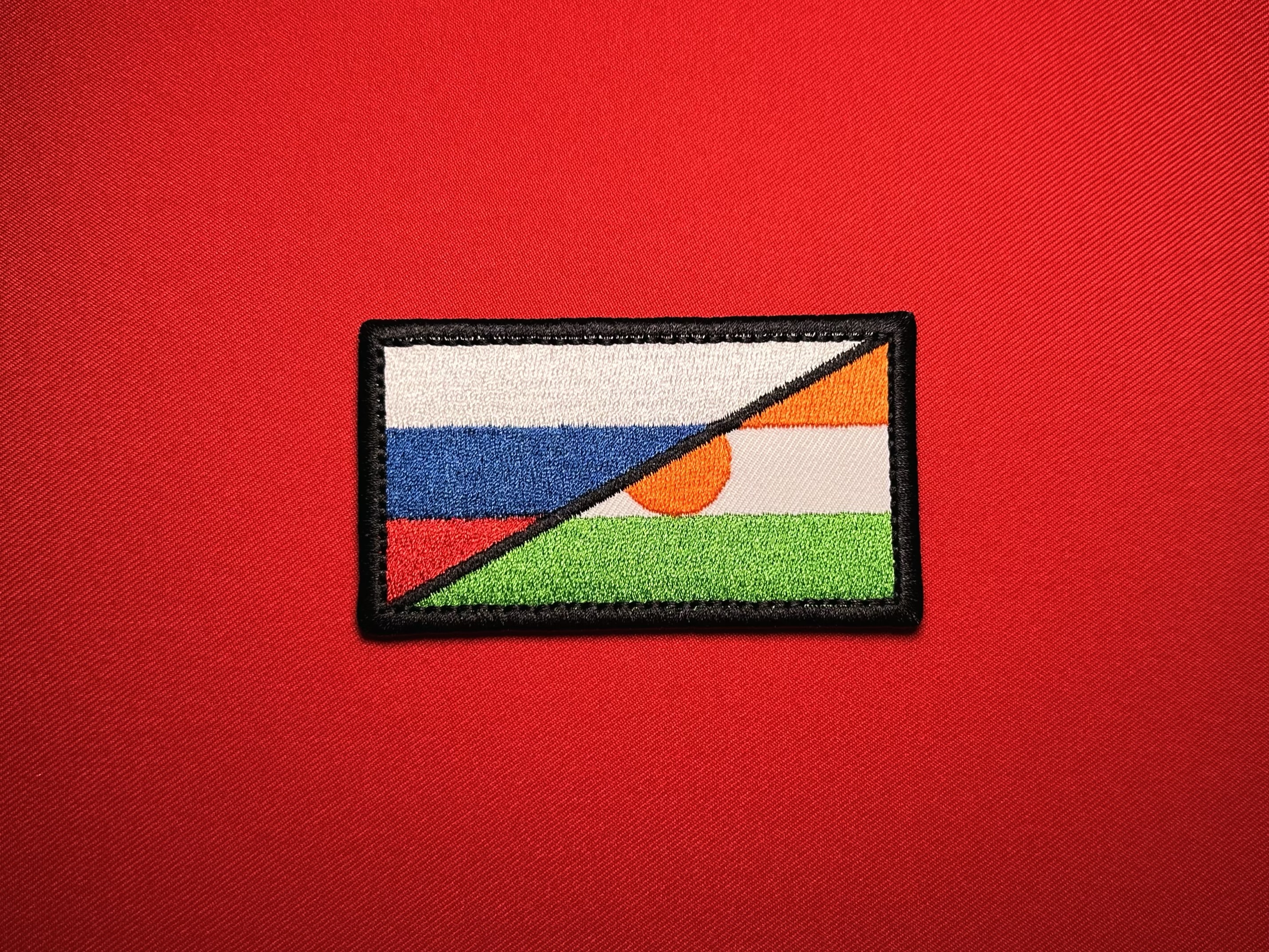 Front view of a Russia–Niger flag replica patch showing the black diagonal divider and partially visible orange Niger disc.