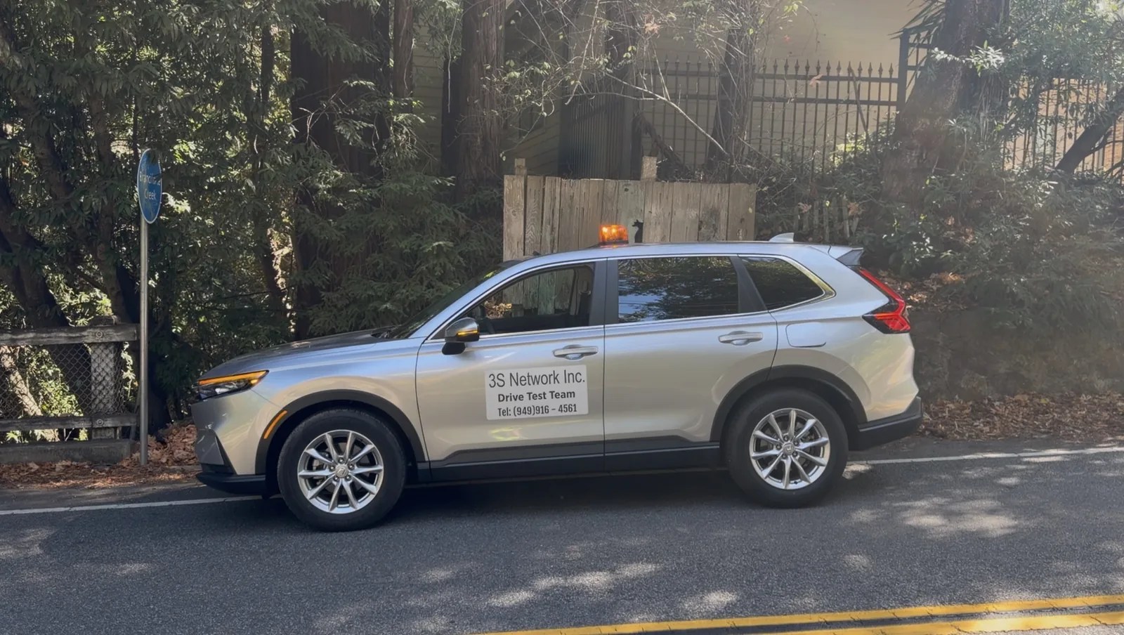3S Network drive test vehicle, a silver SUV with a roof beacon and a "3S Network Inc. Drive Test Team" door sign, parked on a tree-lined road