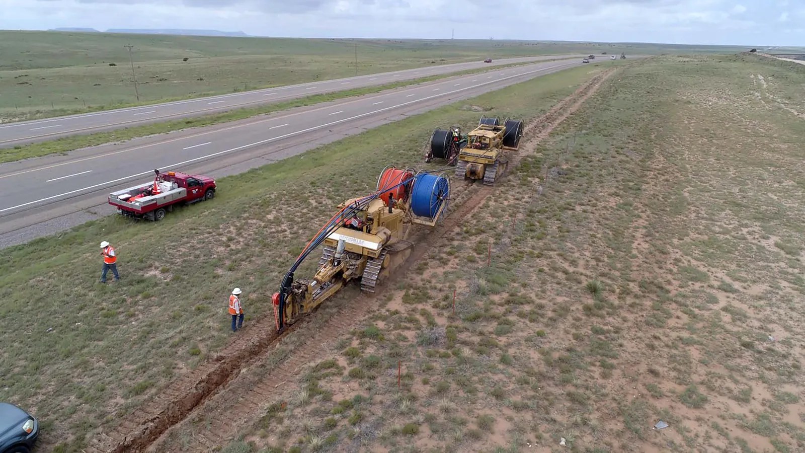 Fiber trenching crew and equipment laying conduit beside a highway