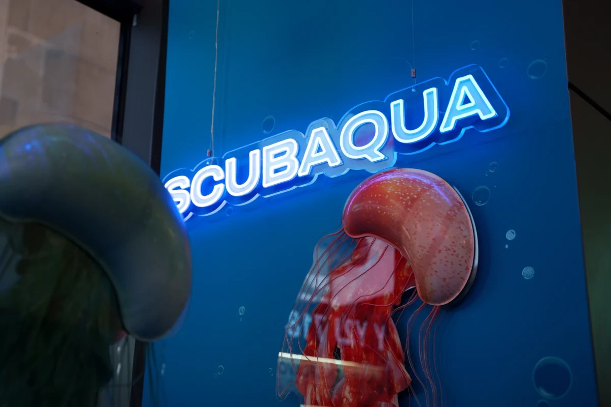 Custom LED neon sign for Swatch Scubaqua retail display with blue illuminated lettering and 3D jellyfish prop on branded wall