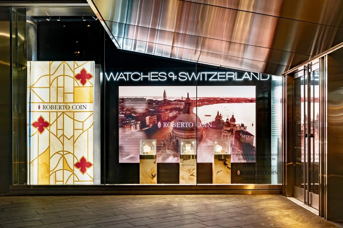 Watches of Switzerland Hudson Yards entrance with neon fascia signage, Roberto Coin LED campaign display, acrylic decorative panel, and marble product pedestals