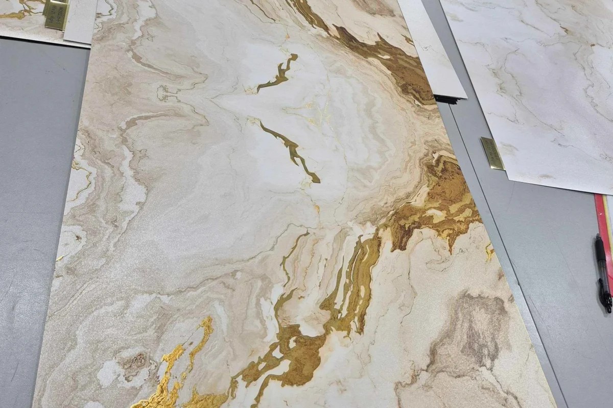 Gold foil adhesive vinyl panels with luxury marble print pattern laid out in a signage production facility for high-end retail display wrapping