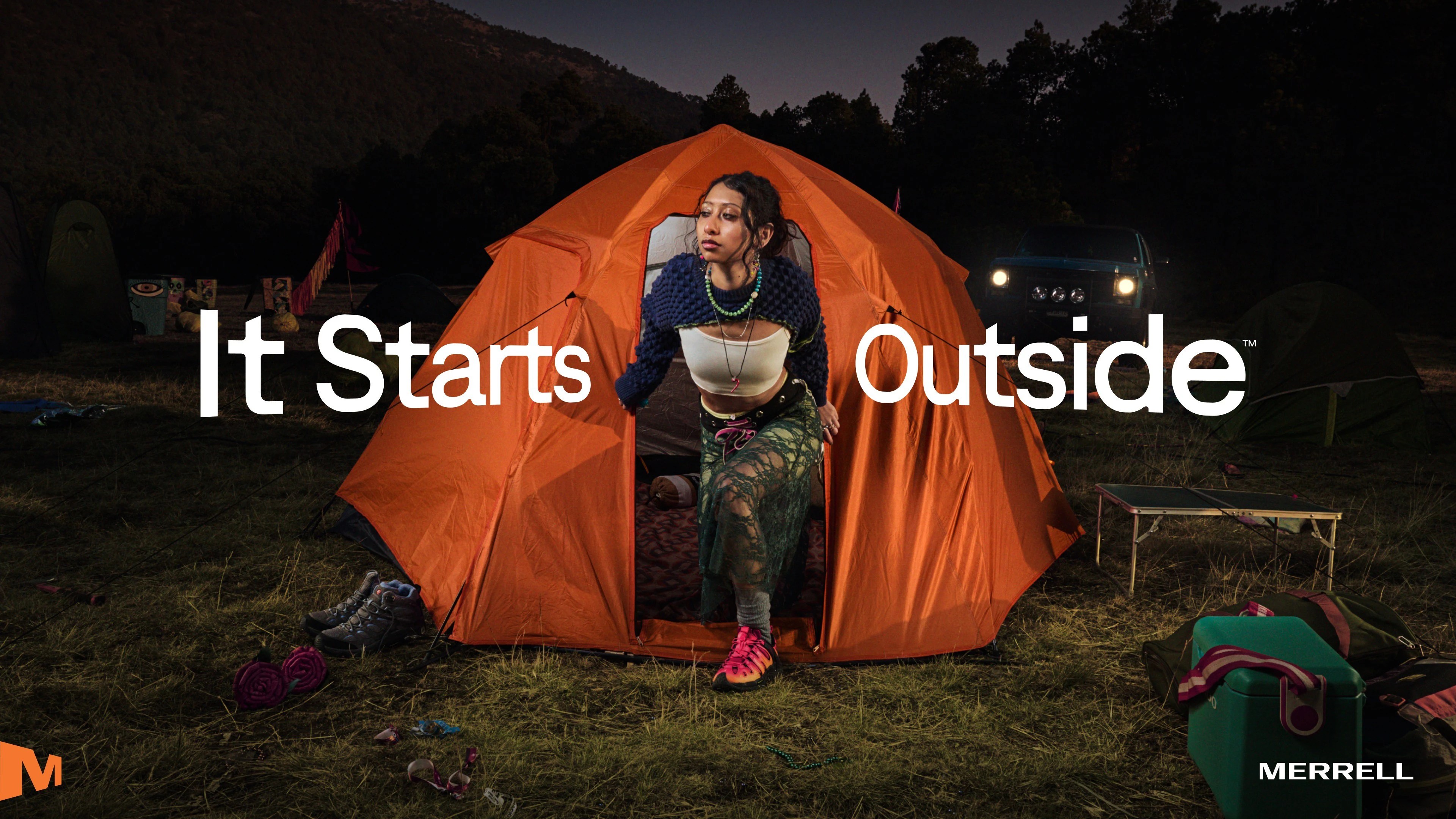 Merrell It Starts Outside campaign image featuring person sitting in orange tent at campsite