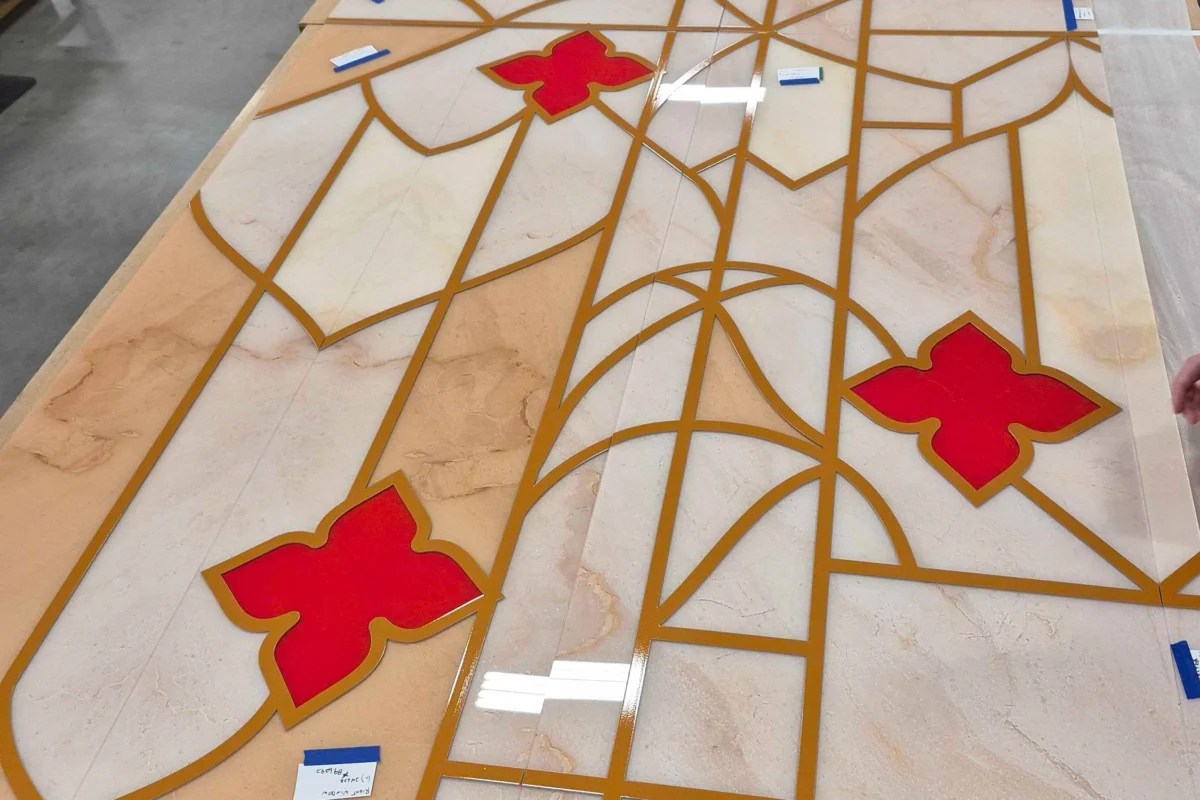 Multiple printed acrylic signage panels assembled in a production facility to form a large-format luxury retail display with gold pattern and red floral elements