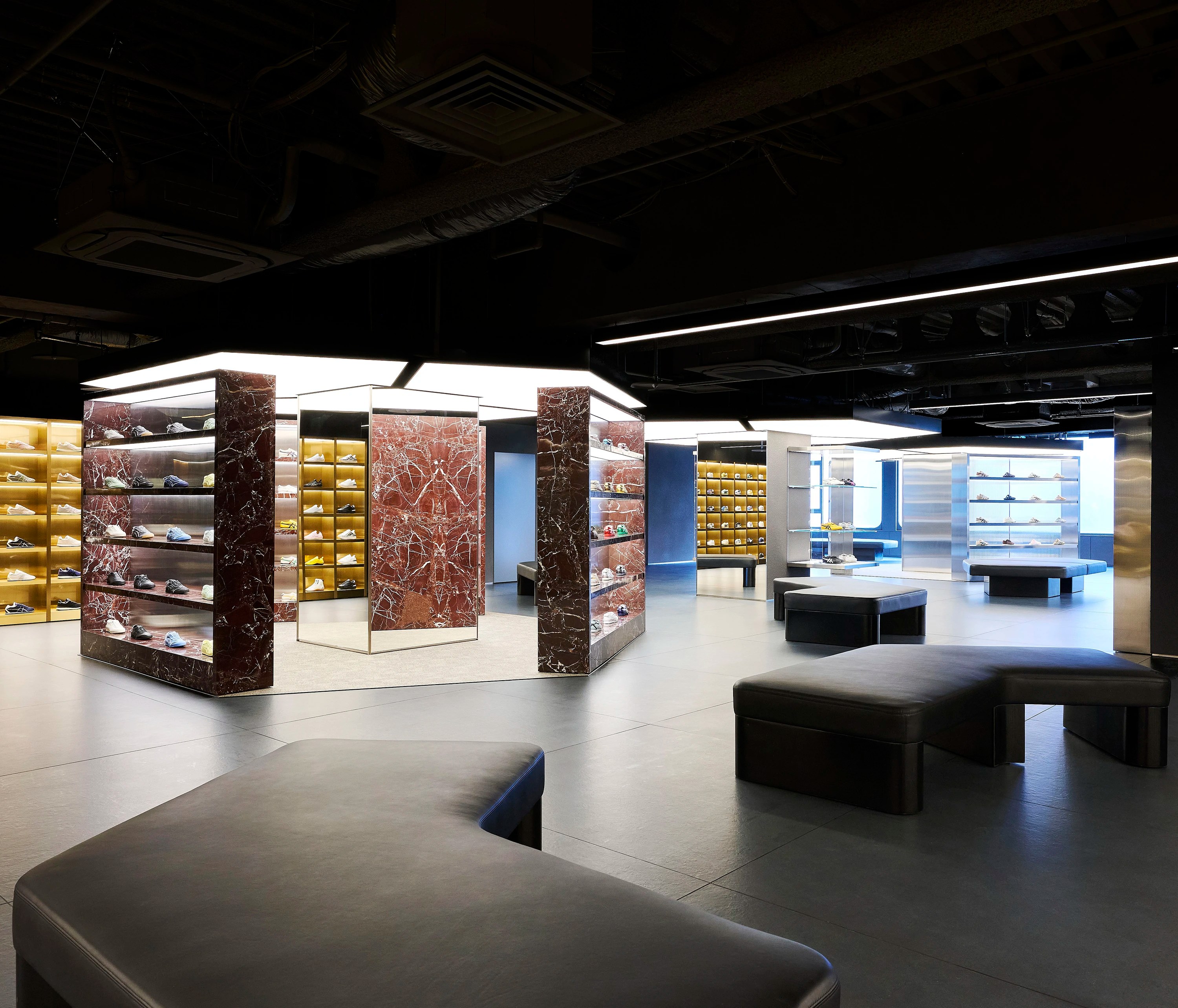 Interior of Onitsuka Tiger's Shinjuku flagship third floor with Rosso Lepanto marble display columns sneaker shelves with gold backlit niches and curved seating