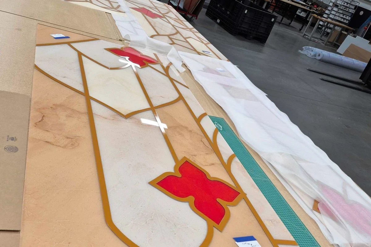 Large-format printed acrylic signage panel with luxury gold and red geometric pattern being assembled in a professional print production facility