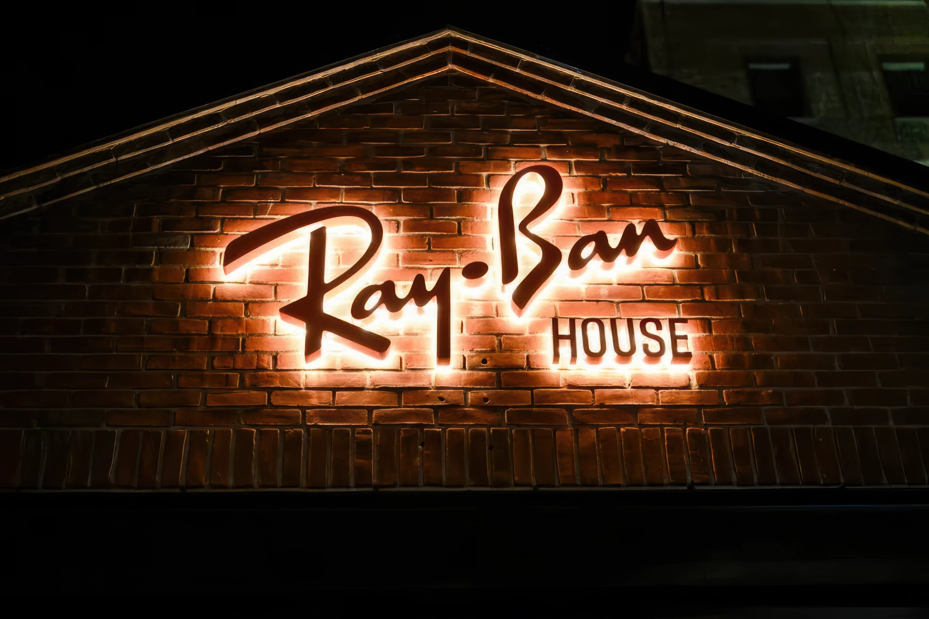 Illuminated Ray-Ban House sign on a brick wall exterior at night in SoHo New York City