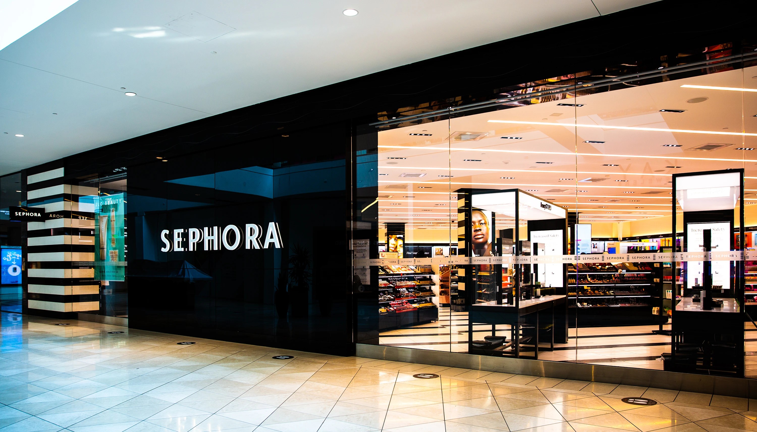 Sephora retail store entrance inside a shopping mall with black glass facade white Sephora signage and beauty product displays visible inside