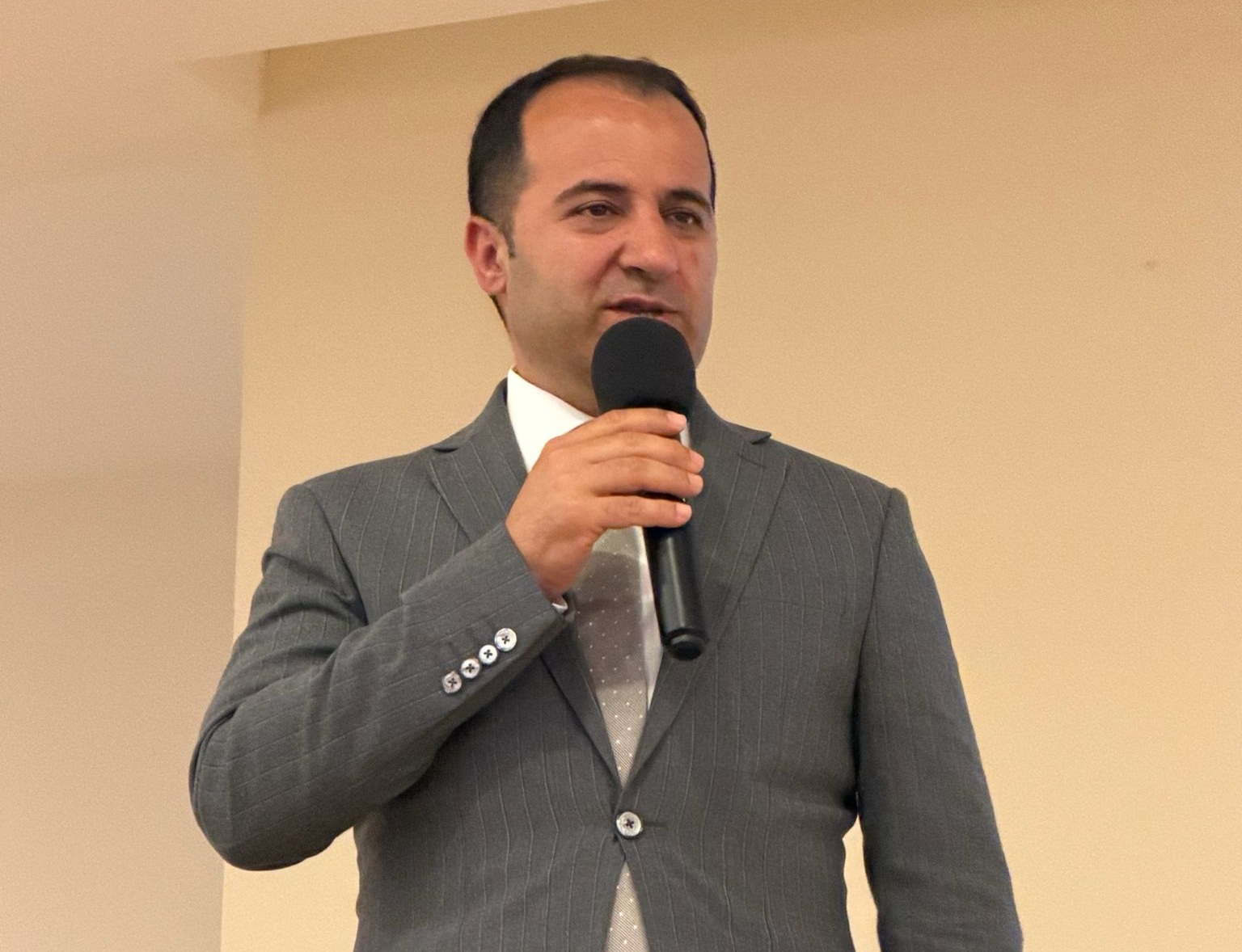 Bir mikrofon tutarak konuşan şık bir adam.