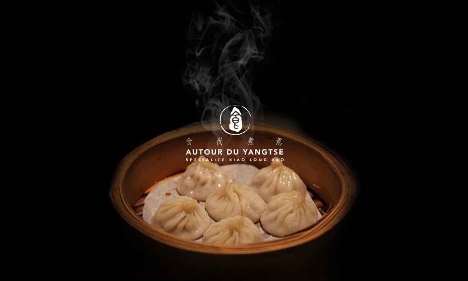A basket of steamed soup dumplings with the words in French indicating it is the specialty of the restaurant Autour de Yangste
