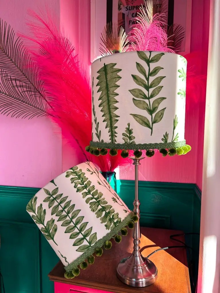 A pair of lampshades in white with a green leaf print.