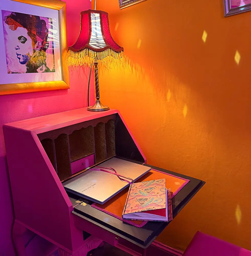 A pink bureau against an orange wall with a flamboyant lamp. 