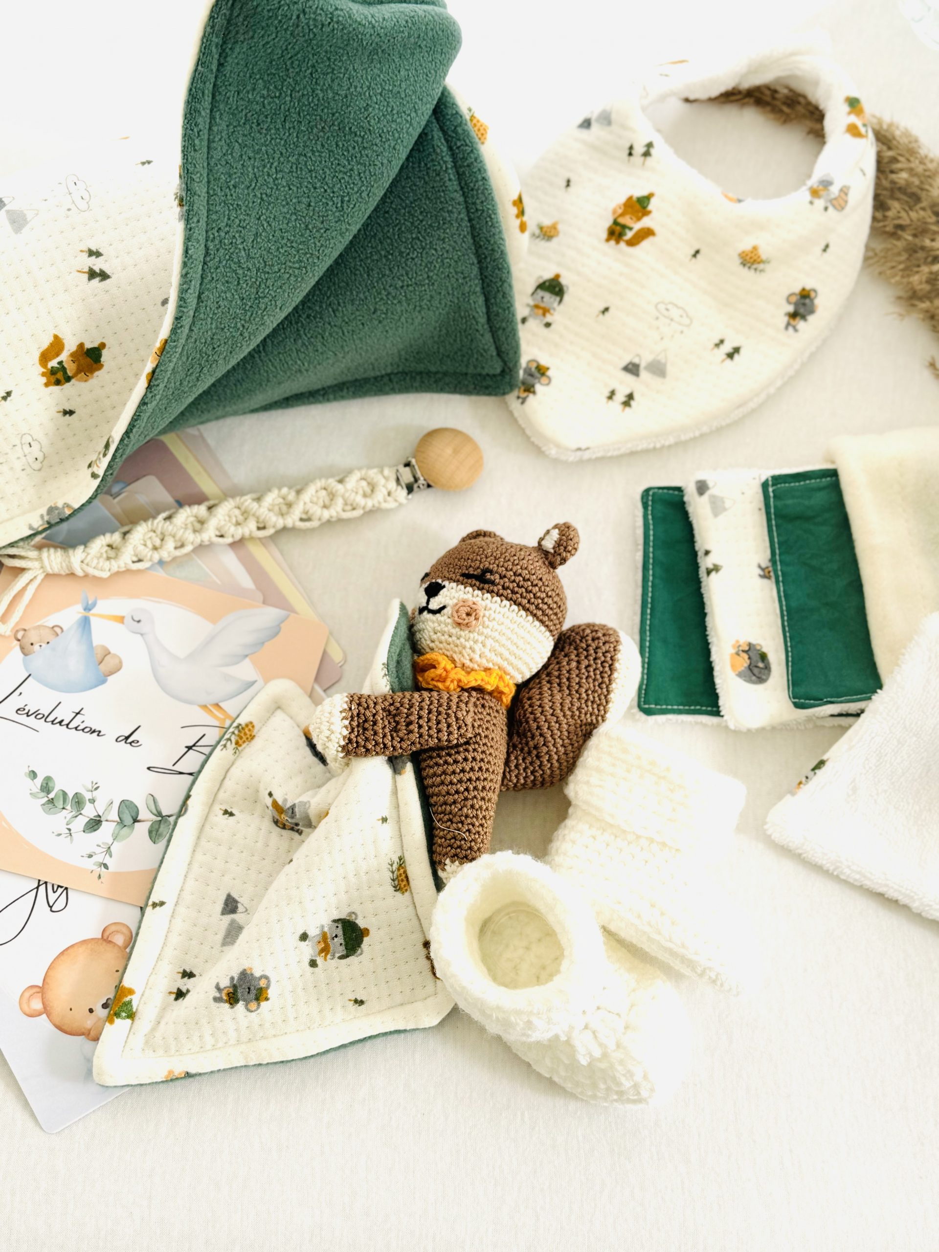 Coffret naissance forêt fait main, aux motifs doux et naturels. Un cadeau artisanal avec doudou, couverture, chaussons, bavoir, lingettes et cartes étapes.