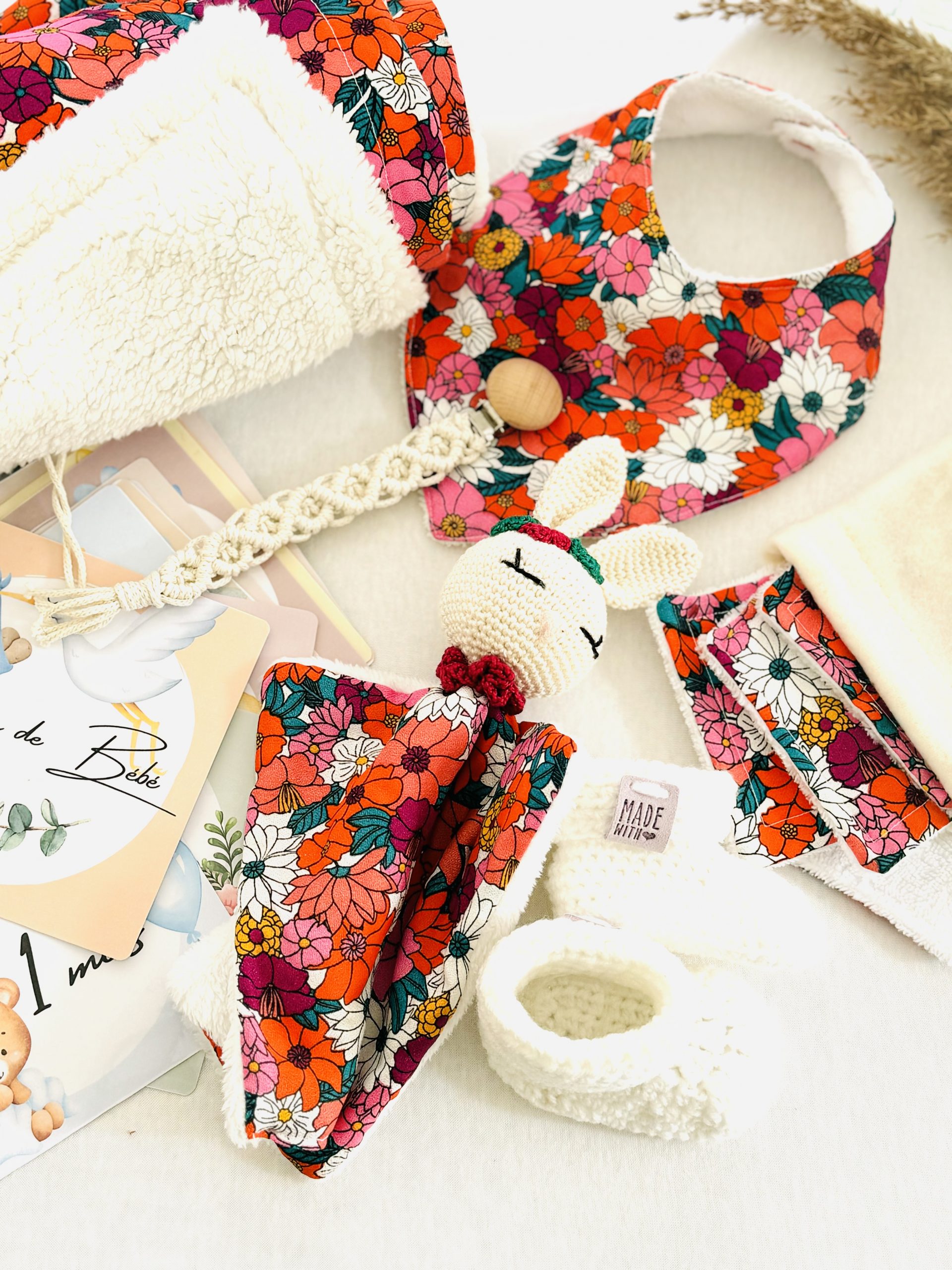 Coffret naissance fleuri artisanal, raffiné et fait main. Inclut couverture, doudou, chaussons, lingettes, bavoir, attache-tétine et cartes étapes.