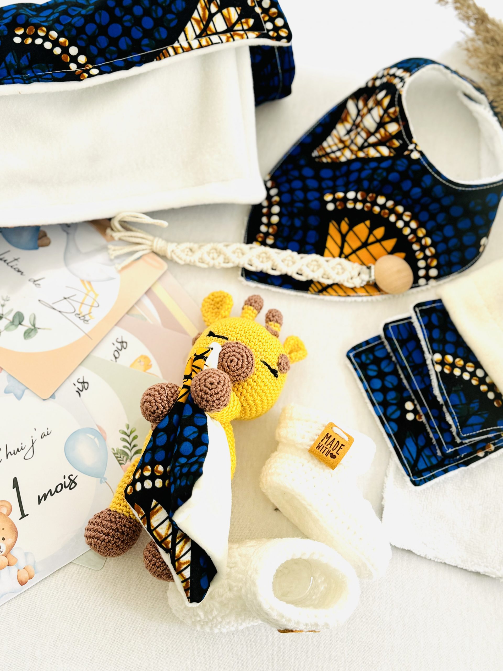 Coffret naissance wax Soleil d’Or : cadeau artisanal et coloré avec doudou, couverture, chaussons, lingettes, bavoir et cartes étapes. Fait main en France.