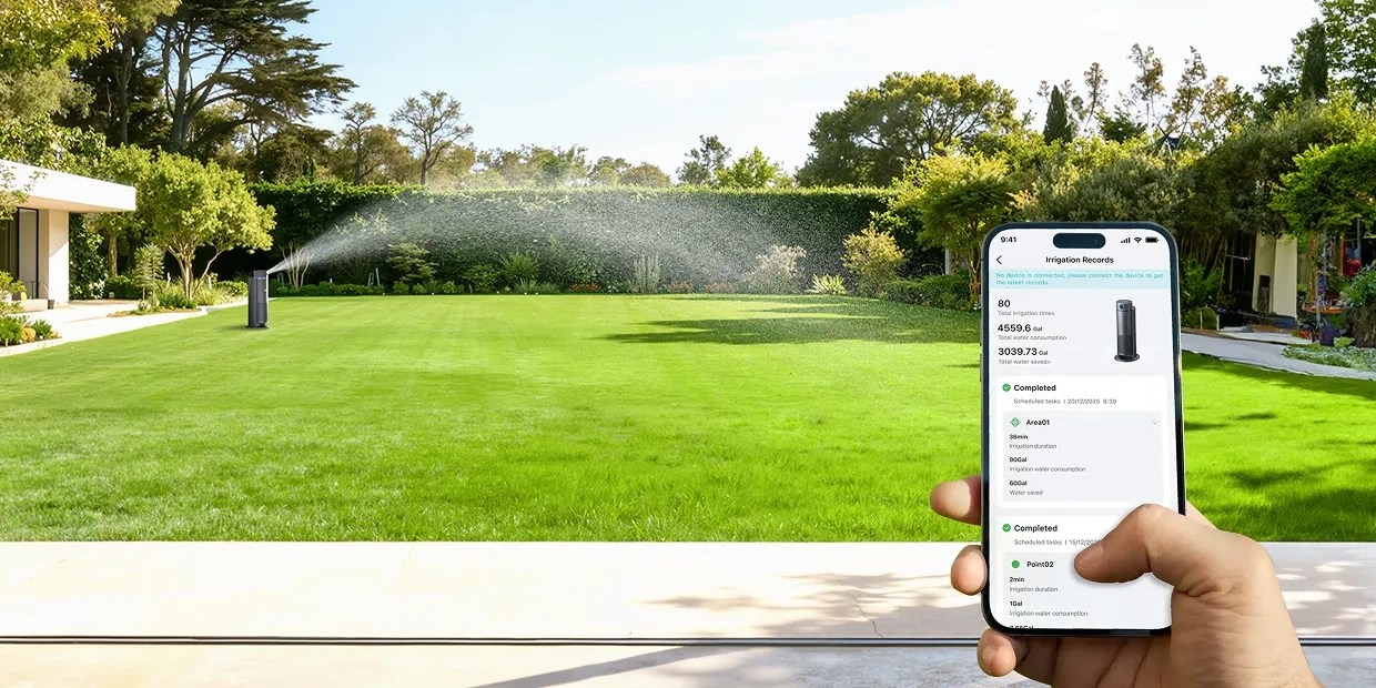 A person holding a phone with a sprinkler spraying water on a lawn