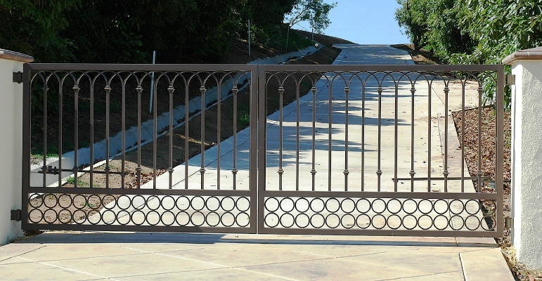 Black ornamental iron double driveway gate with scrollwork along the lower rail