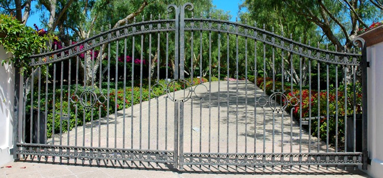 Dark gray arched double iron gate across a sloped driveway