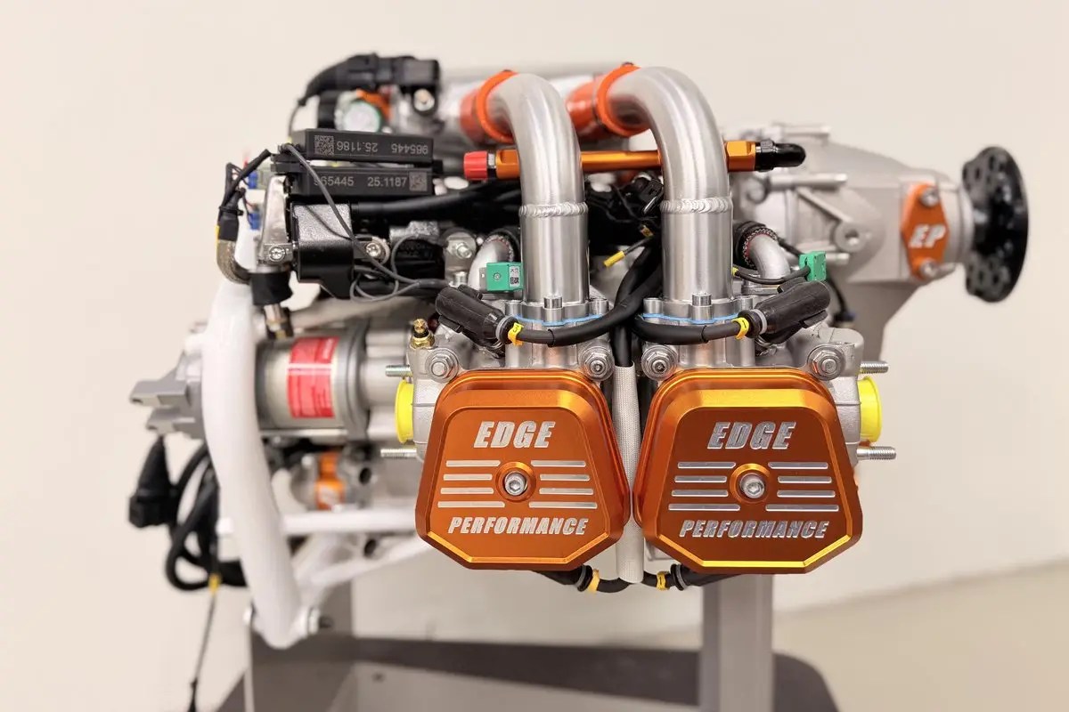 Close-up of a car engine with twin orange air intake covers labeled EDGE PERFORMANCE and silver tubing above them.